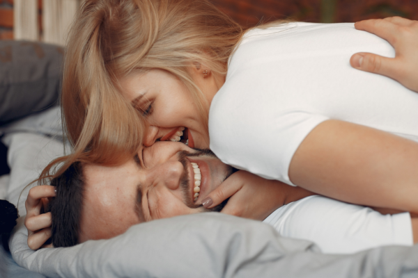Par som ler og er nær hverandre i sengen – viser hvordan gnisten og nærheten i forhold kan vekkes igjen