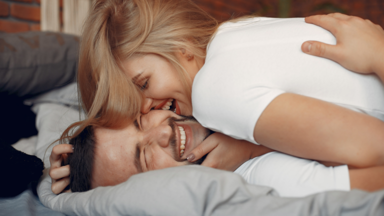 Par som ler og er nær hverandre i sengen – viser hvordan gnisten og nærheten i forhold kan vekkes igjen